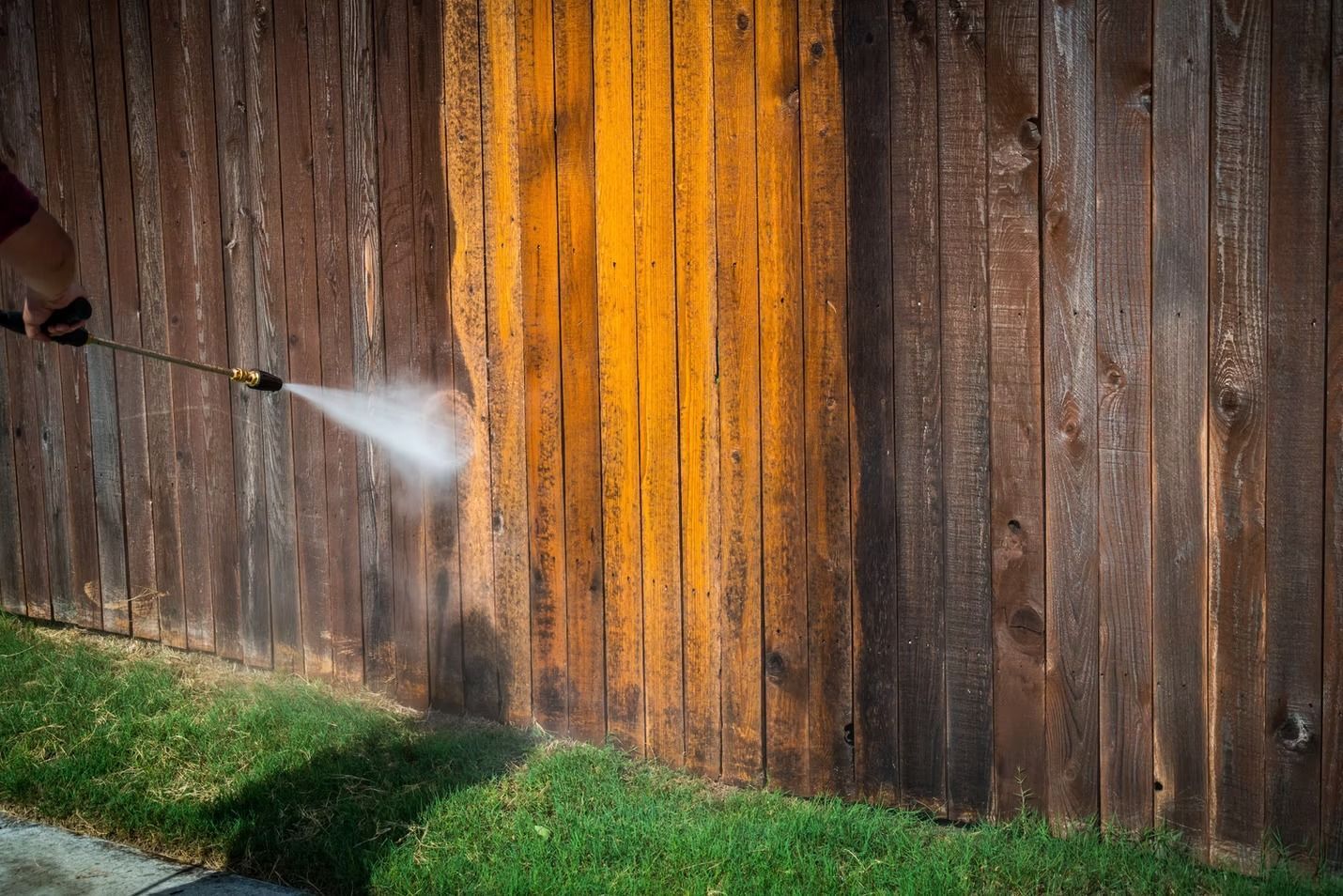Water spraying from a hose onto a weathered wooden fence beside green grass
