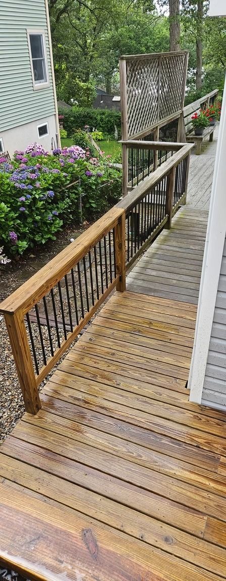 Wooden ramp with railing beside a house, surrounded by greenery and flowers.