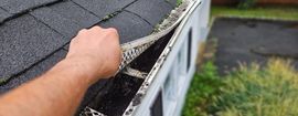 Hand lifting damaged shingle on a roof edge, exposing rotten wood underneath