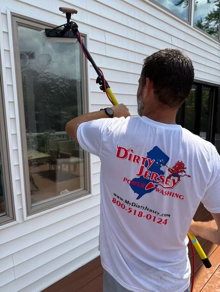 Worker using a long pole to clean an upstairs window on a house exterior.