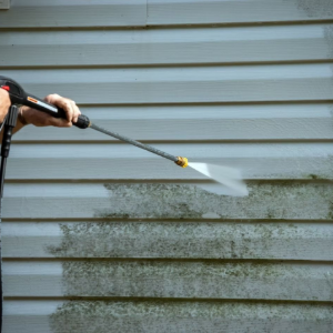 Person pressure-washing dirty gray house siding with a spray wand