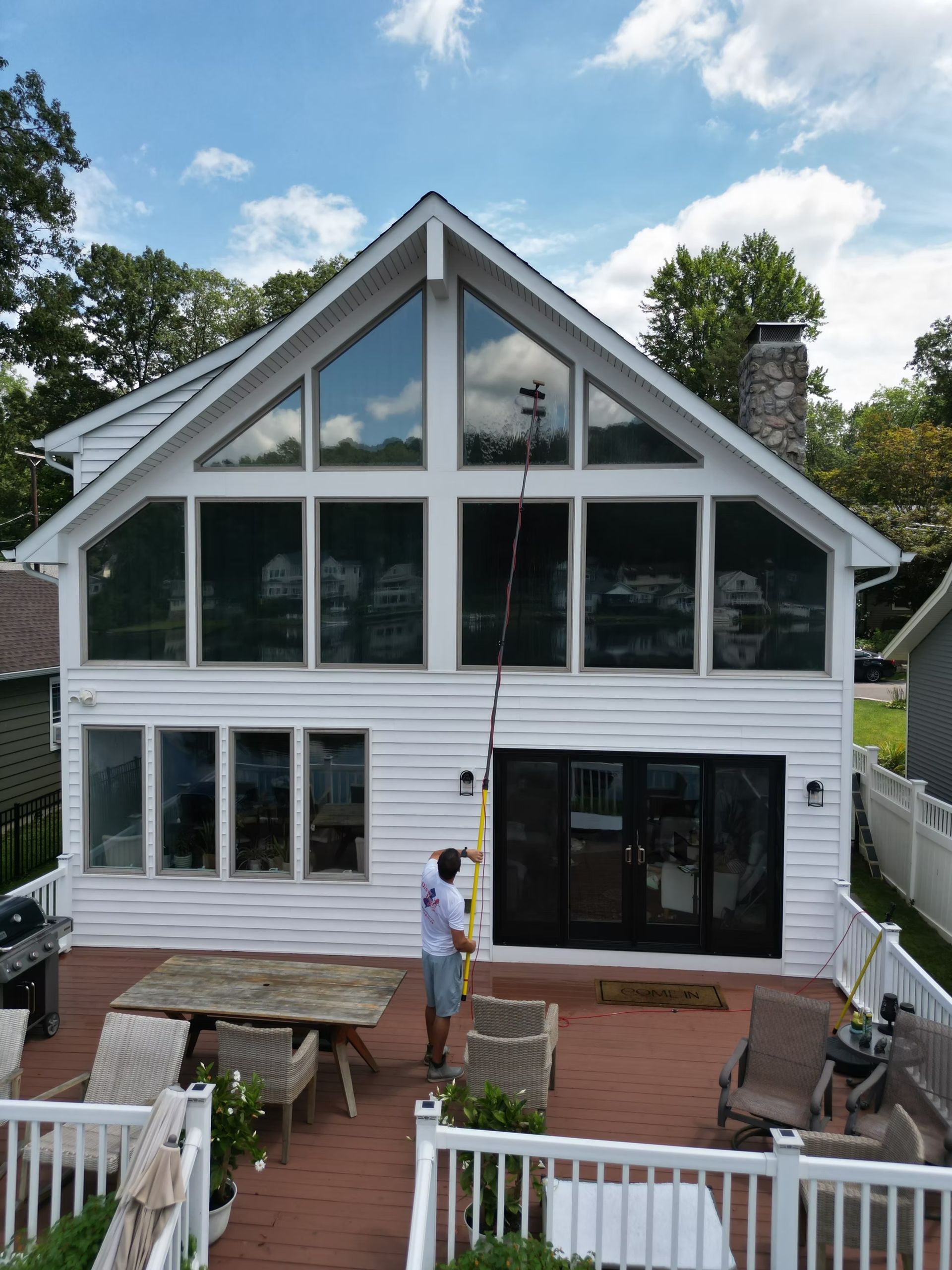 White two-story house with large windows, deck, and a person standing outside under a blue sky