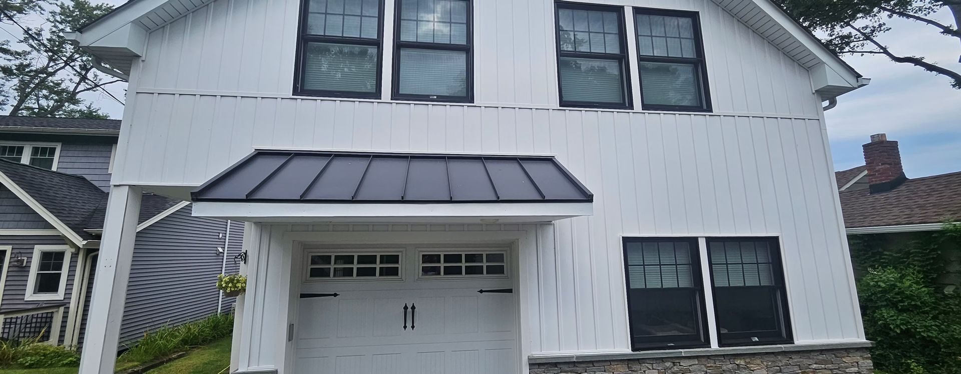 White two-story house exterior with black-trim windows and a small covered garage entrance