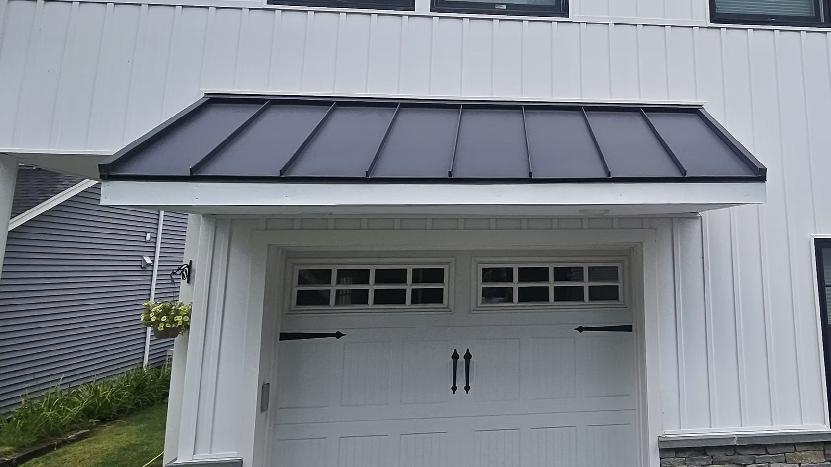 White garage with a black metal awning and white double doors on a house exterior