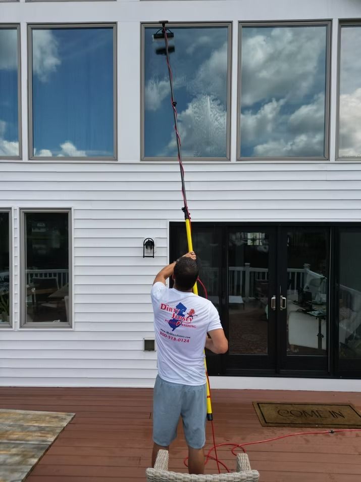 Person power washing the exterior of a white building with windows and a glass door.