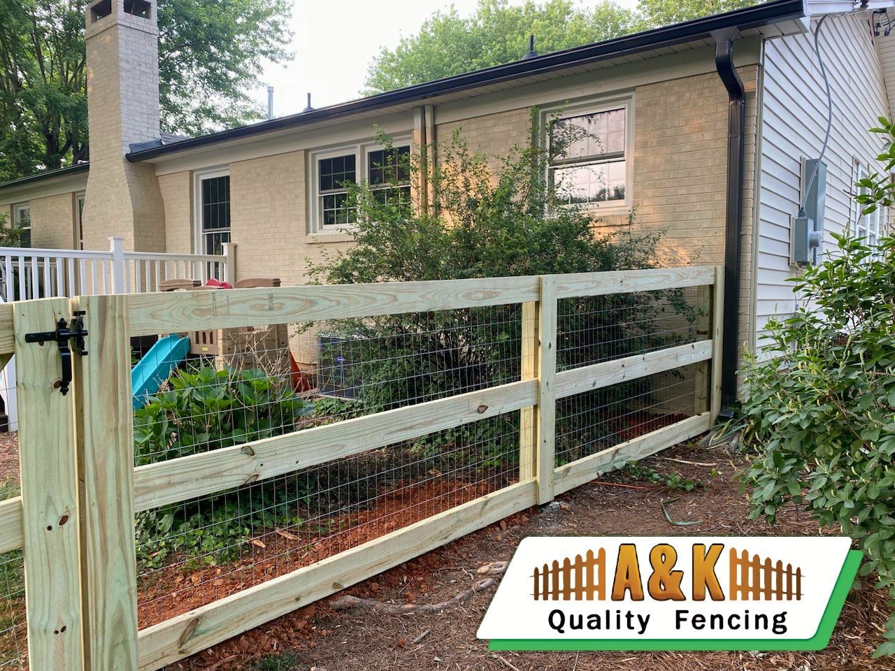 Wooden fence in front of a house, with black hardware. The ground has brown mulch.