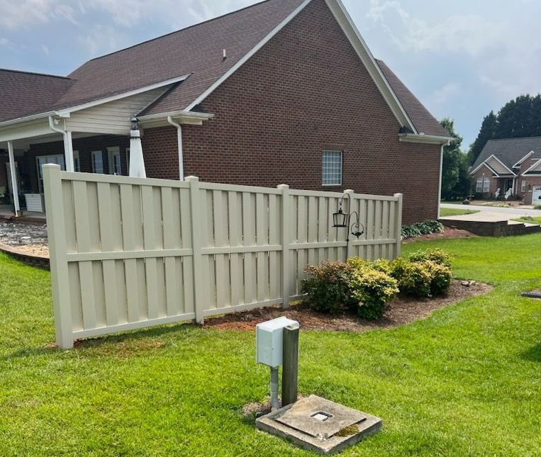 Tan fence surrounds a grassy yard, brick house in background.