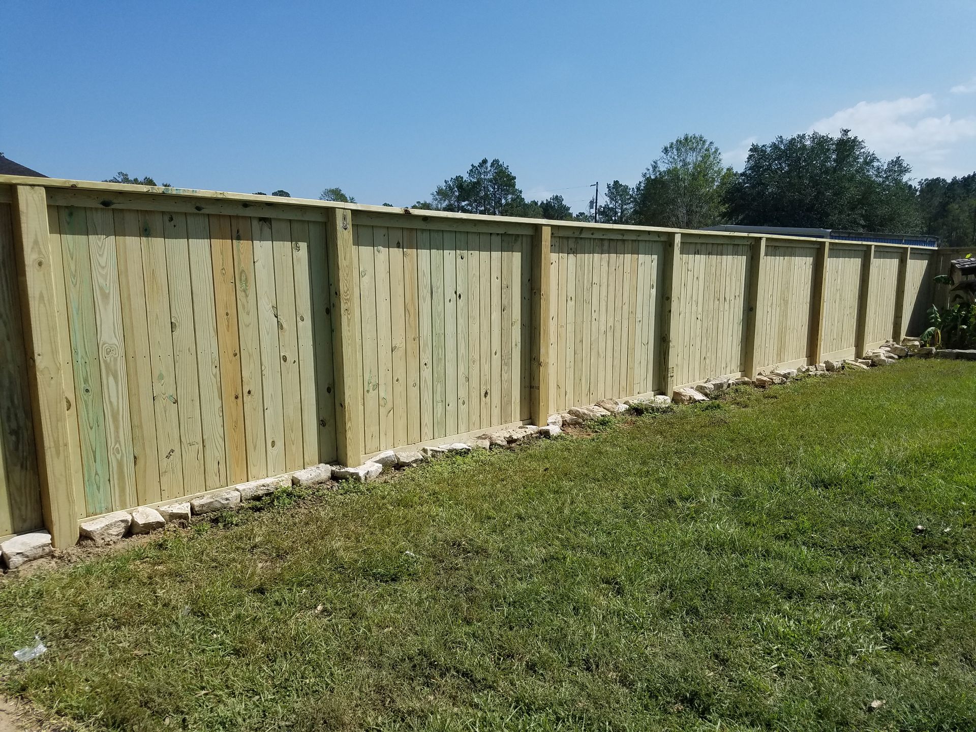 A wooden fence in a grassy yard under a blue sky.