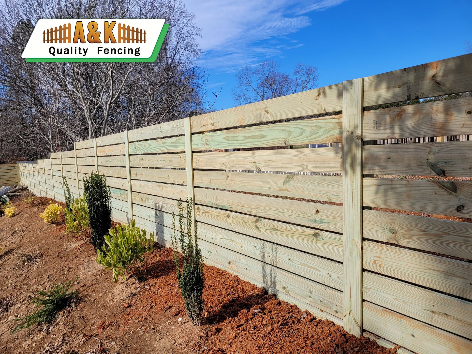 Wooden privacy fence with landscaping against a blue sky.