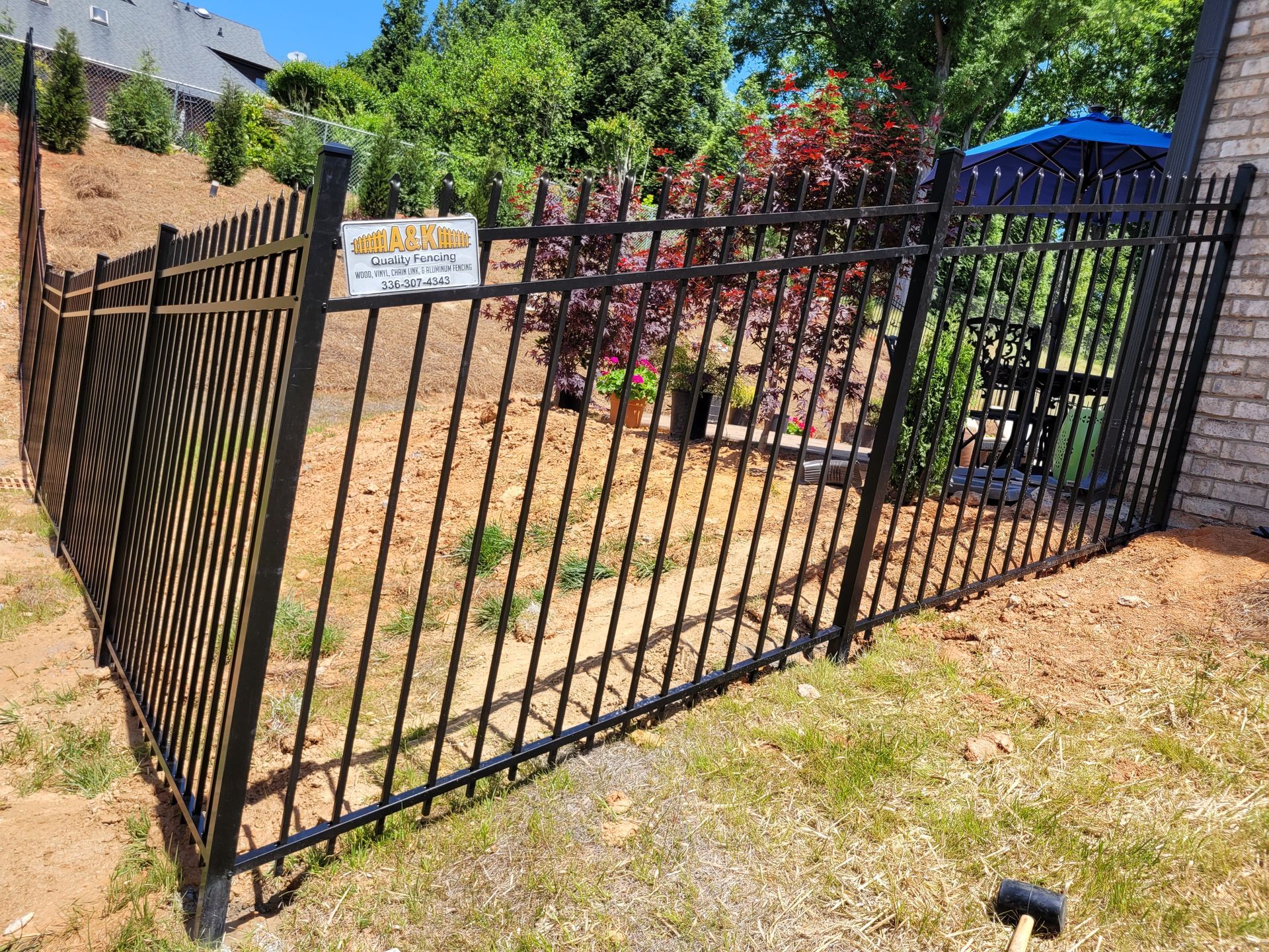 Black metal fence bordering a yard with landscaping. A small sign is attached to the fence.