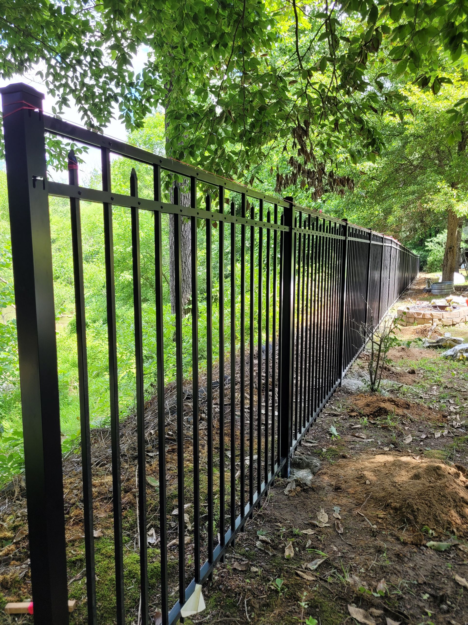 Black metal fence in a wooded area.