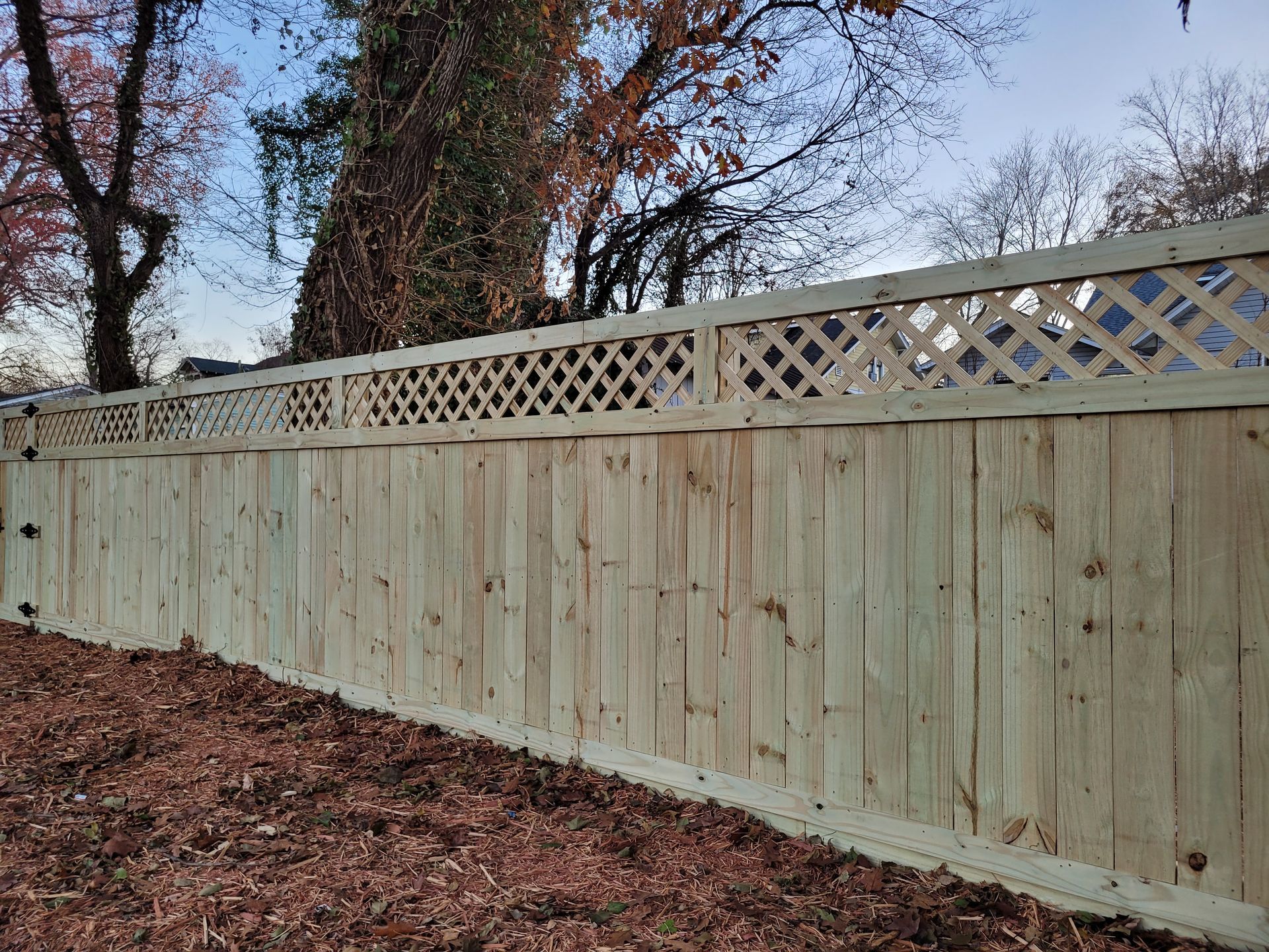 Wooden fence with lattice top, in front of bare trees and blue sky.