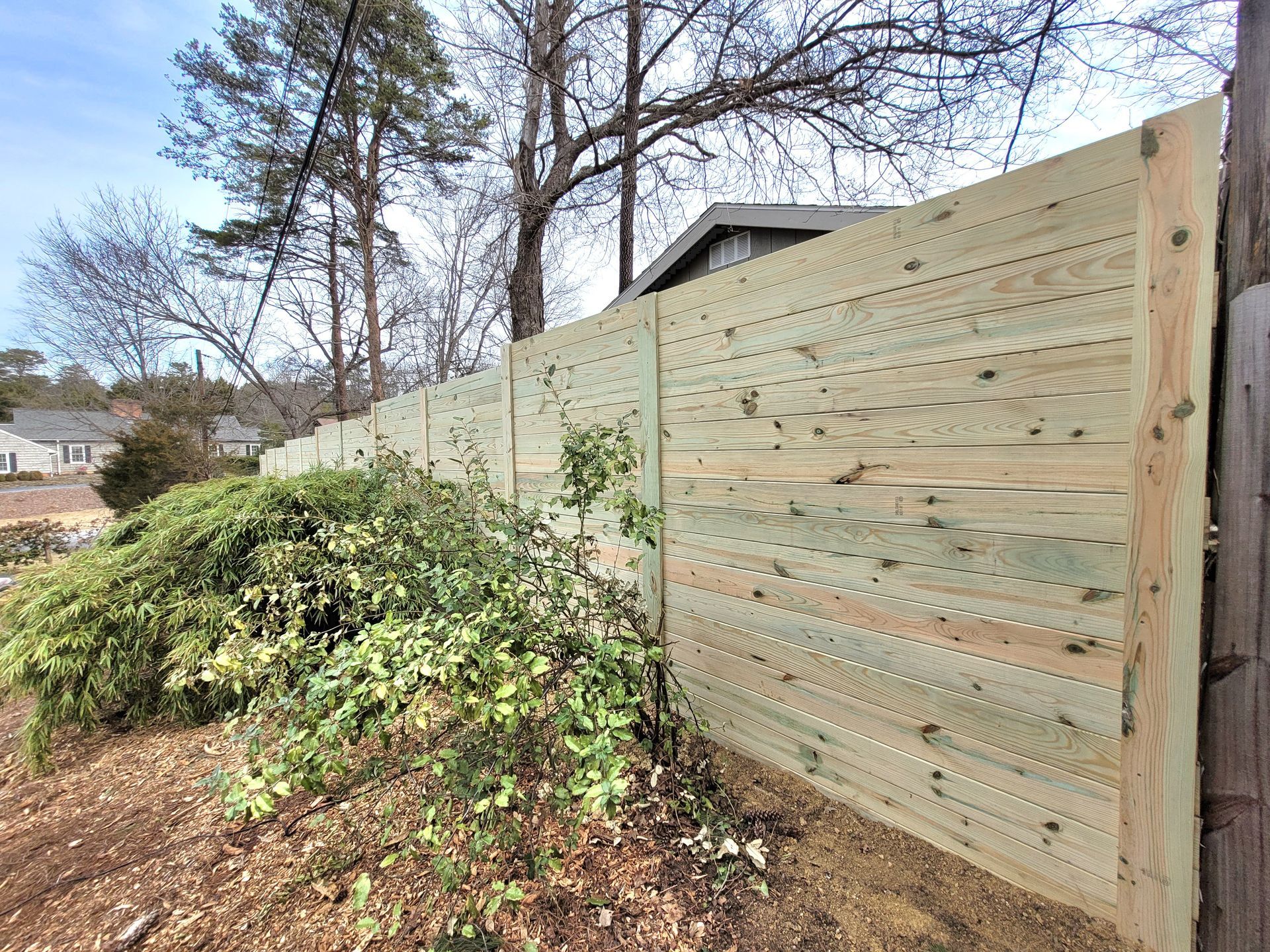 Wooden privacy fence with shrubbery in front of it.