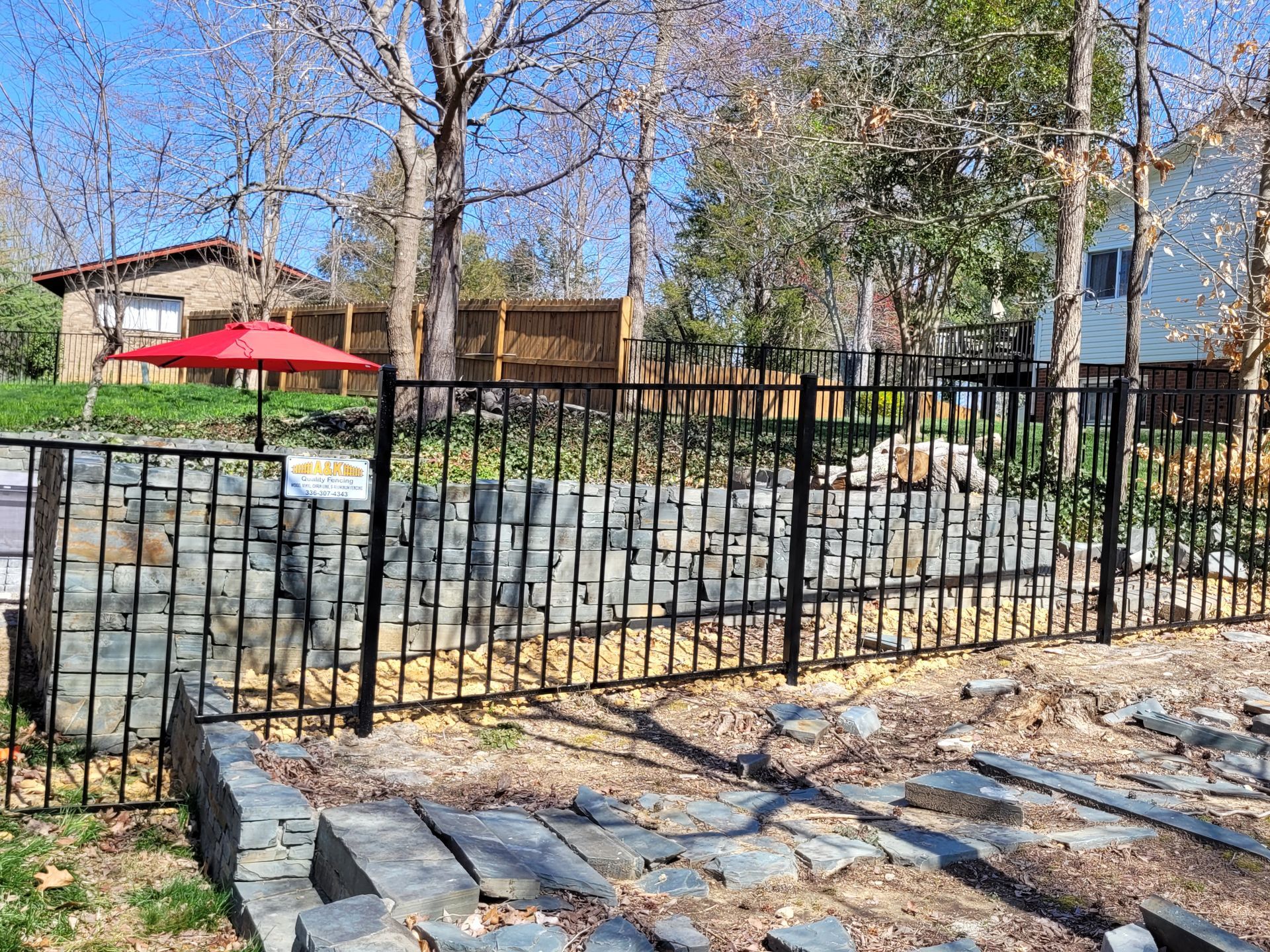 Black metal fence in front of a stone wall. A red umbrella and houses are in the background.