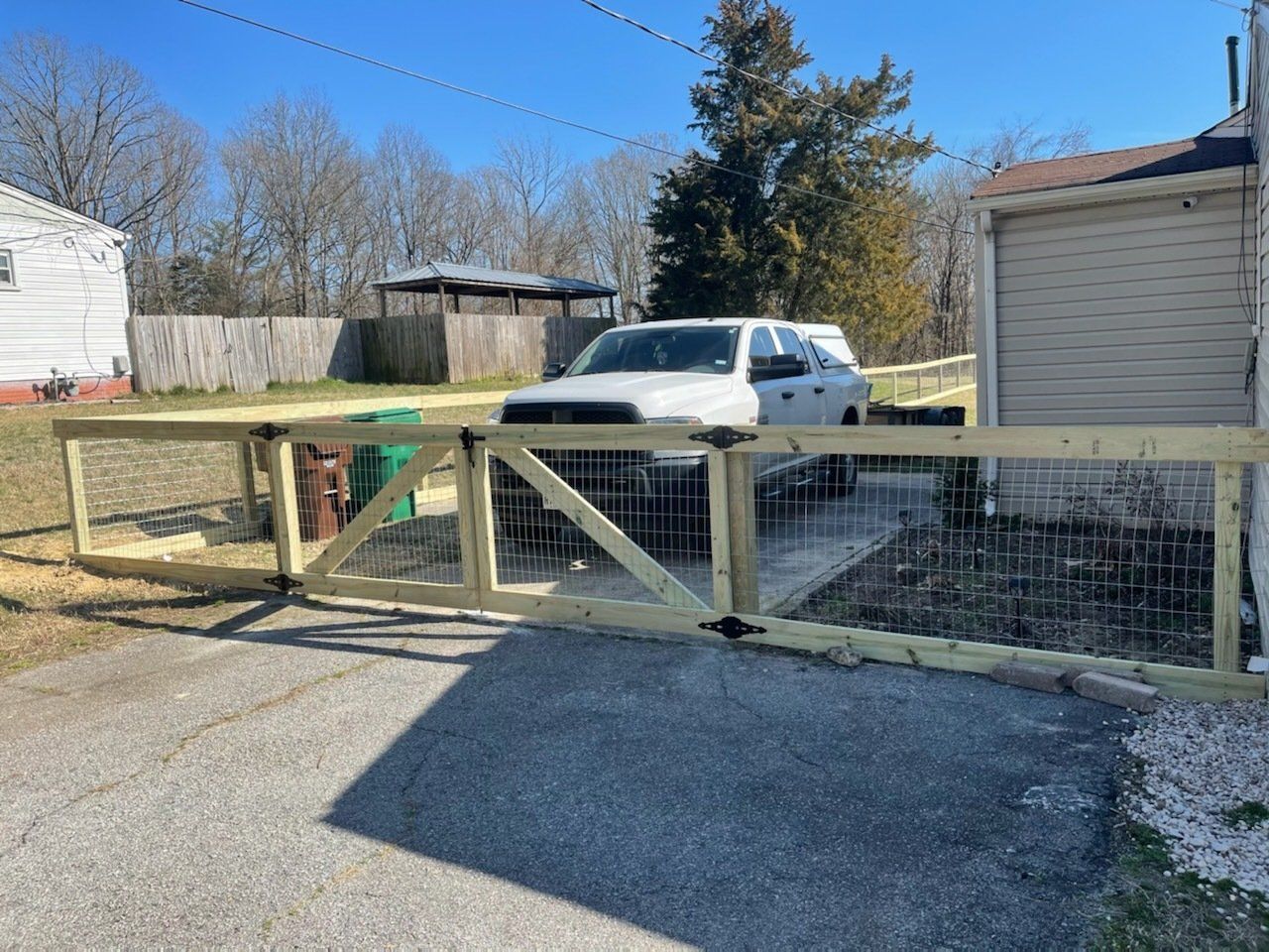 Wooden gate with metal mesh, driveway, white SUV, and suburban houses.
