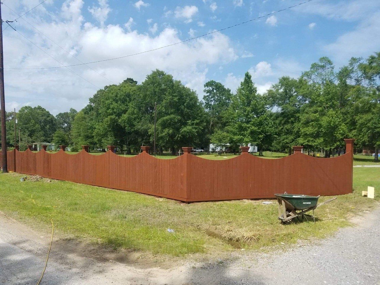 Brown wooden fence surrounds a grassy area, with trees and a blue sky in the background.