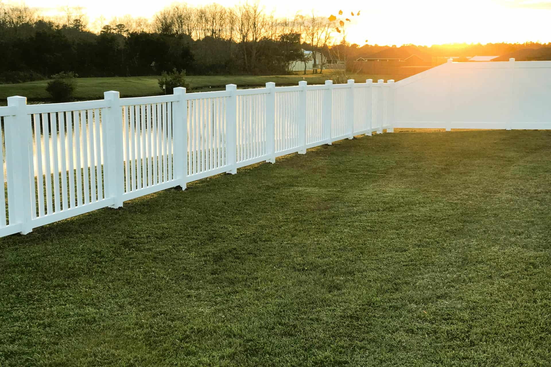 White picket fence on green lawn, setting sun in the background.