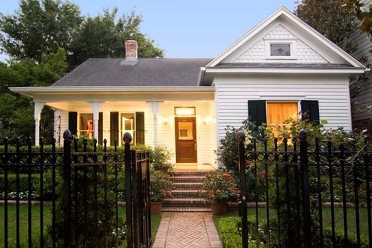 White house with black shutters, brick path, and wrought iron fence.