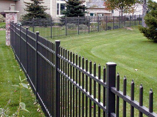 Black metal fence bordering a green lawn in front of houses.
