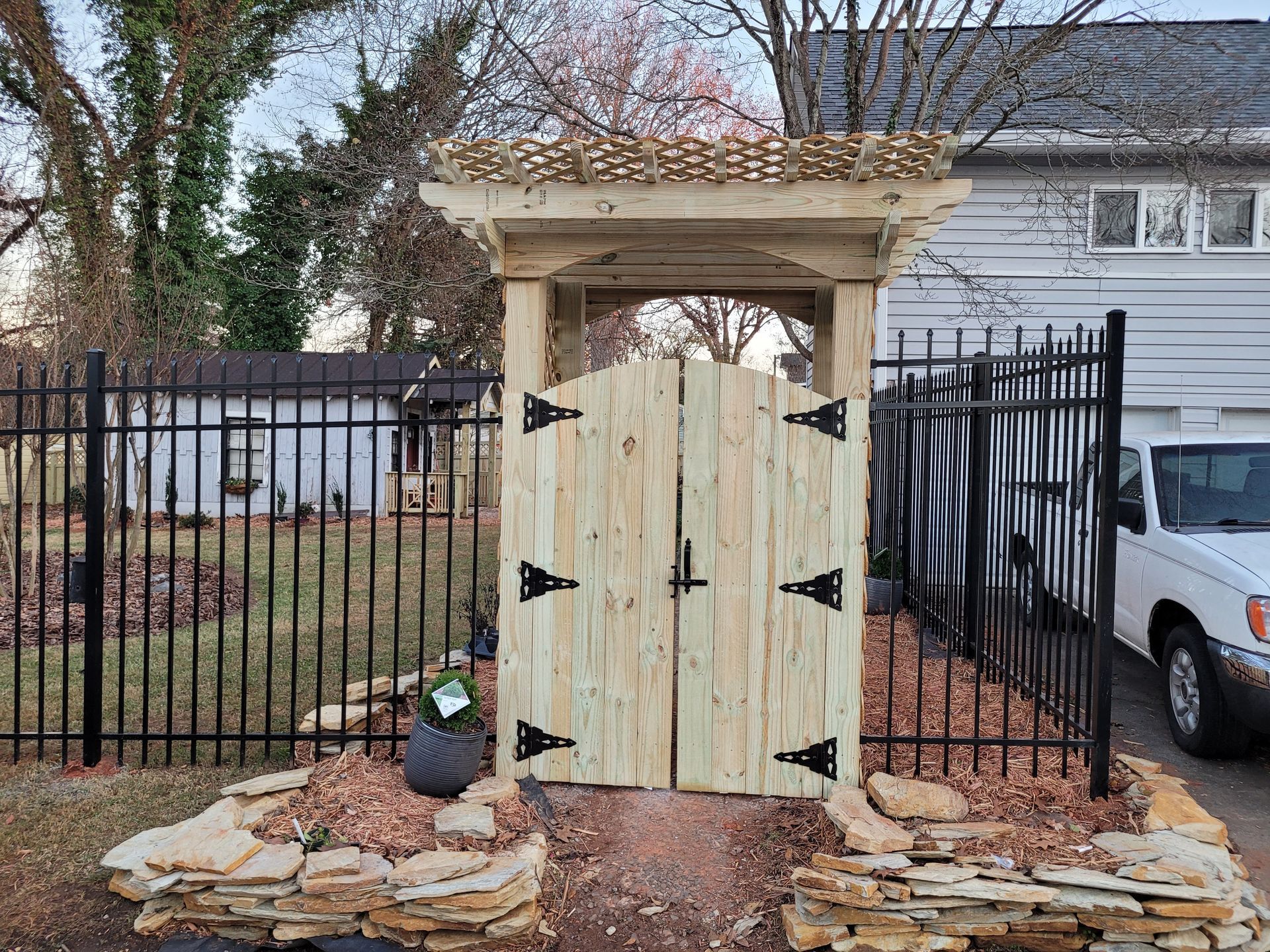 Wooden gate with arched top, surrounded by black metal fence and stone landscaping.