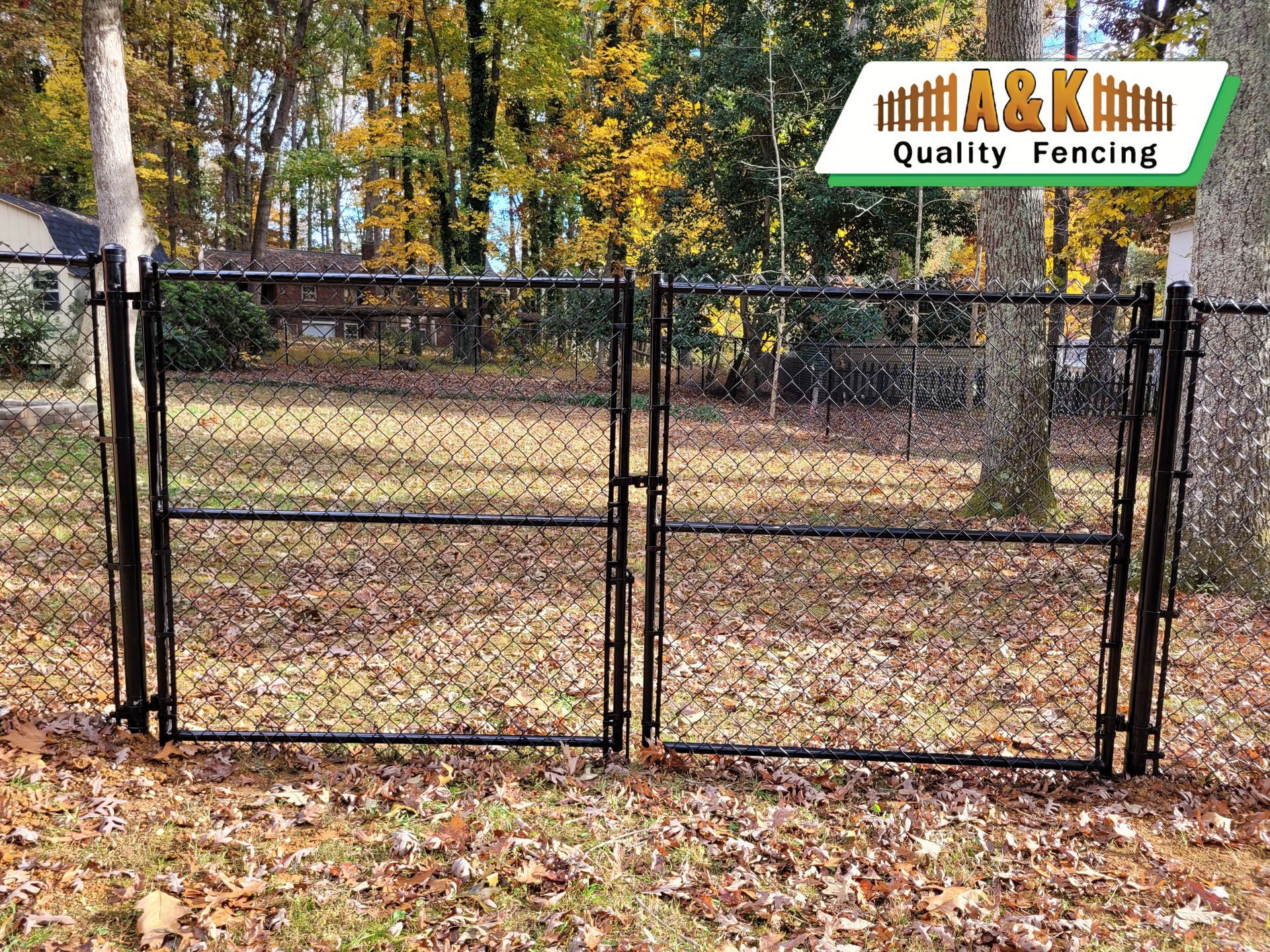 Black chain-link double gate in a yard with fall leaves.