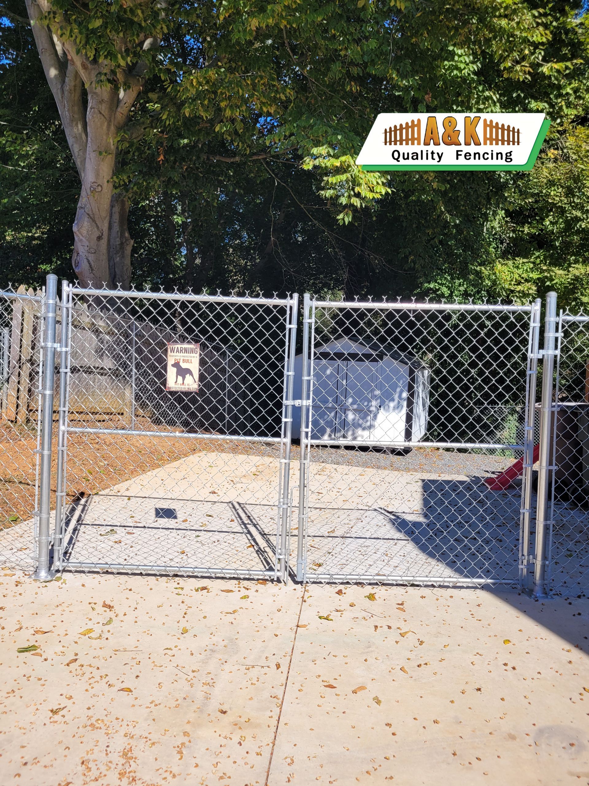 Two chain-link gates, a warning sign, and a concrete path. Trees in the background.