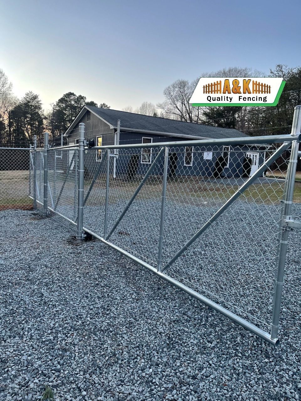 Metal fence in front of a dark building, set on gravel. Evening light.