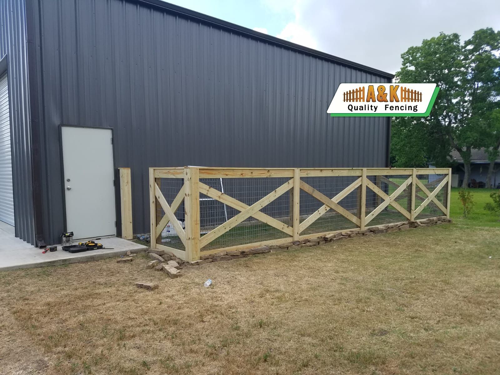 Wooden fence with wire mesh in front of a dark gray building.