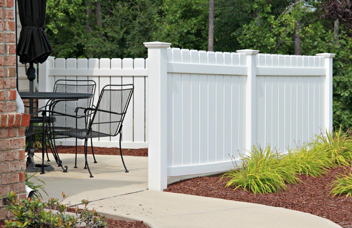 White vinyl fence surrounding a patio with black metal furniture and an umbrella.