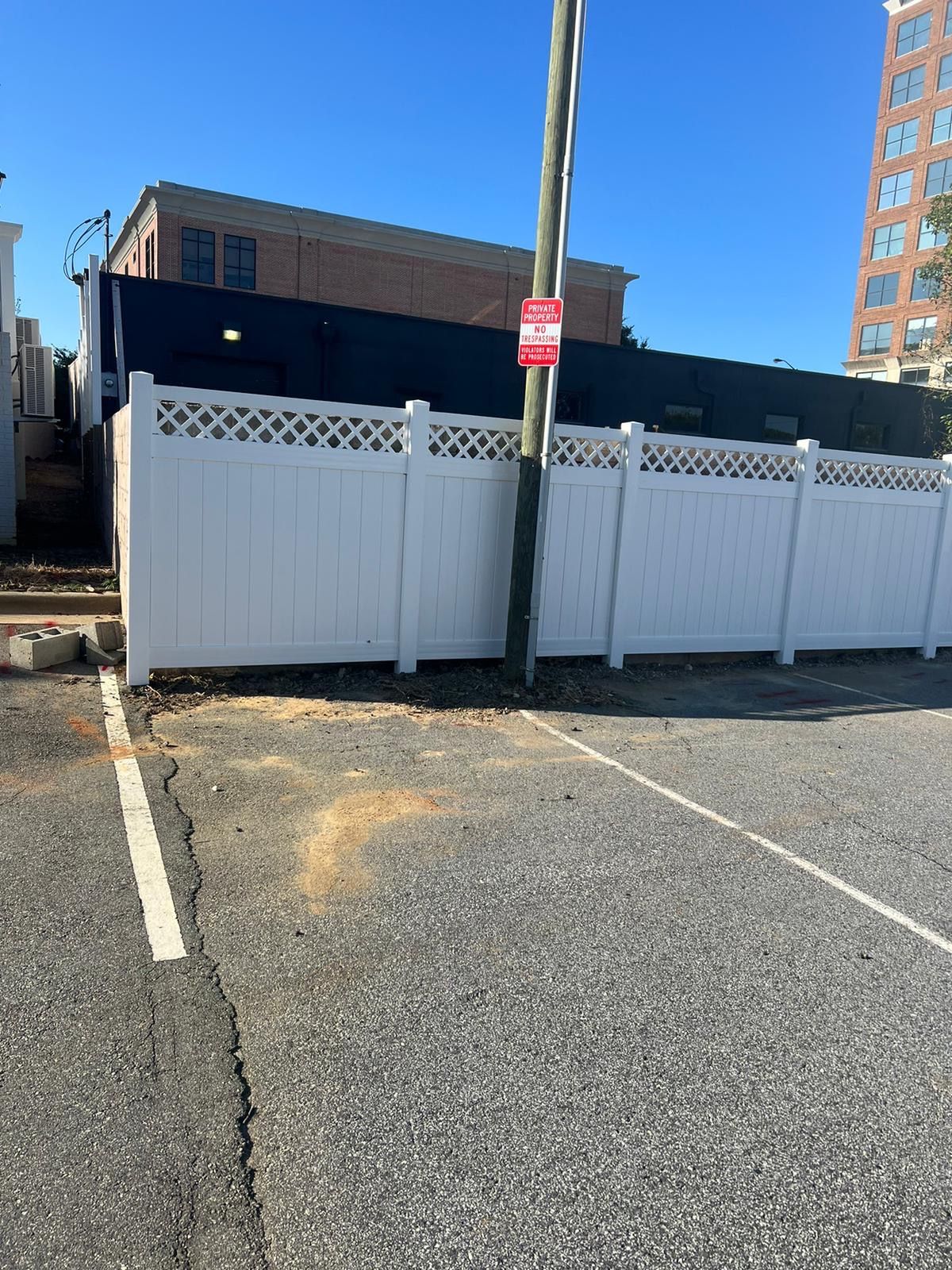 White fence and utility pole on asphalt, with a building in the background under a blue sky.