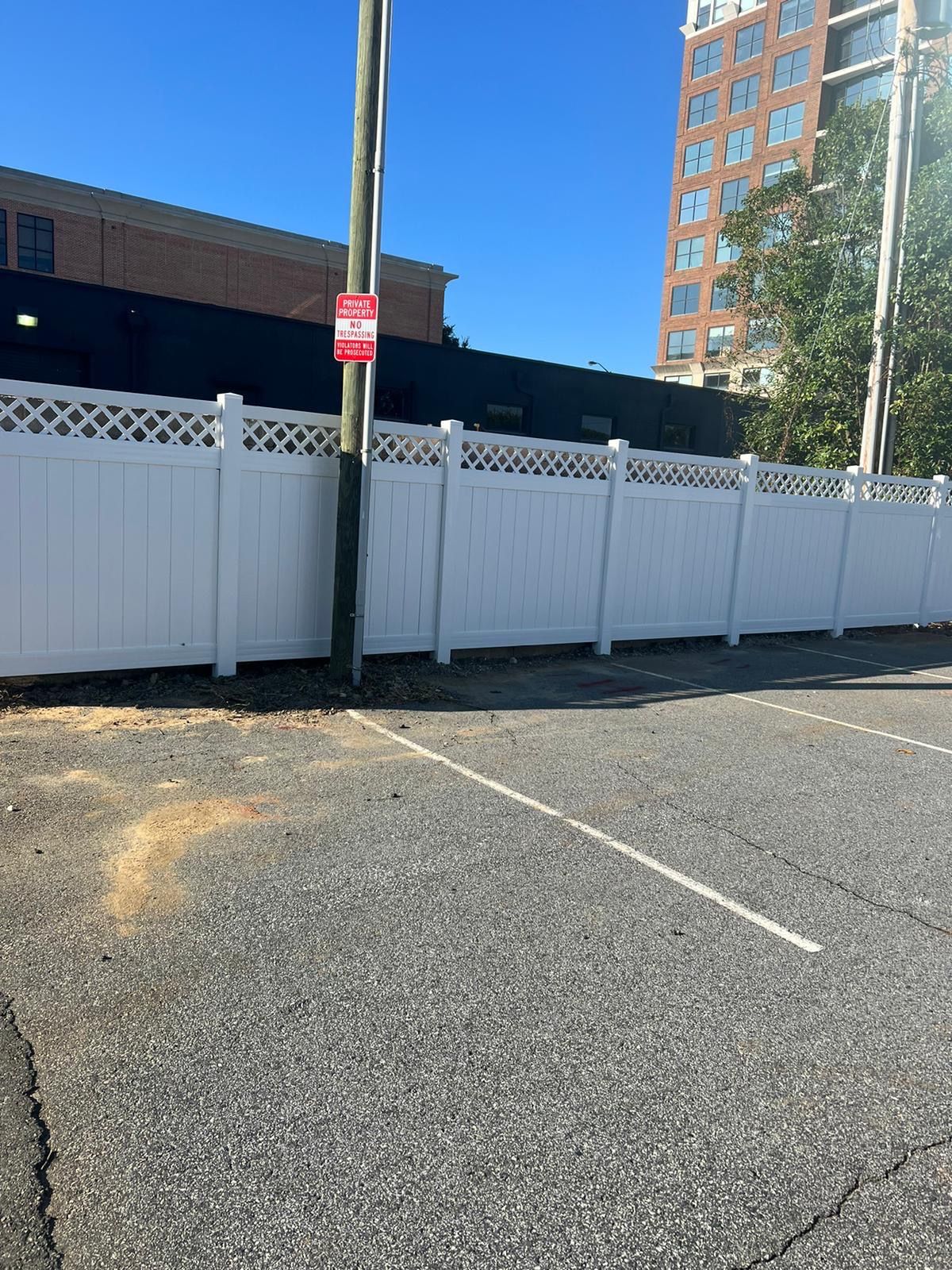White fence borders a parking lot with a utility pole and a building on a sunny day.