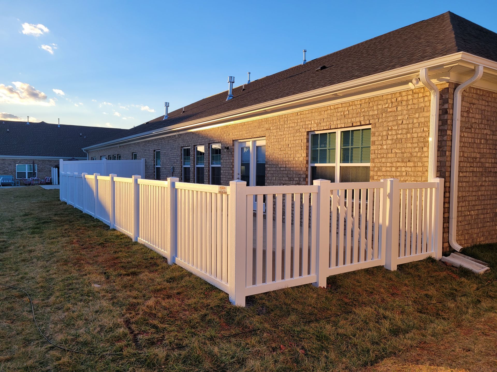 White picket fence surrounding a small patio next to a brick building.