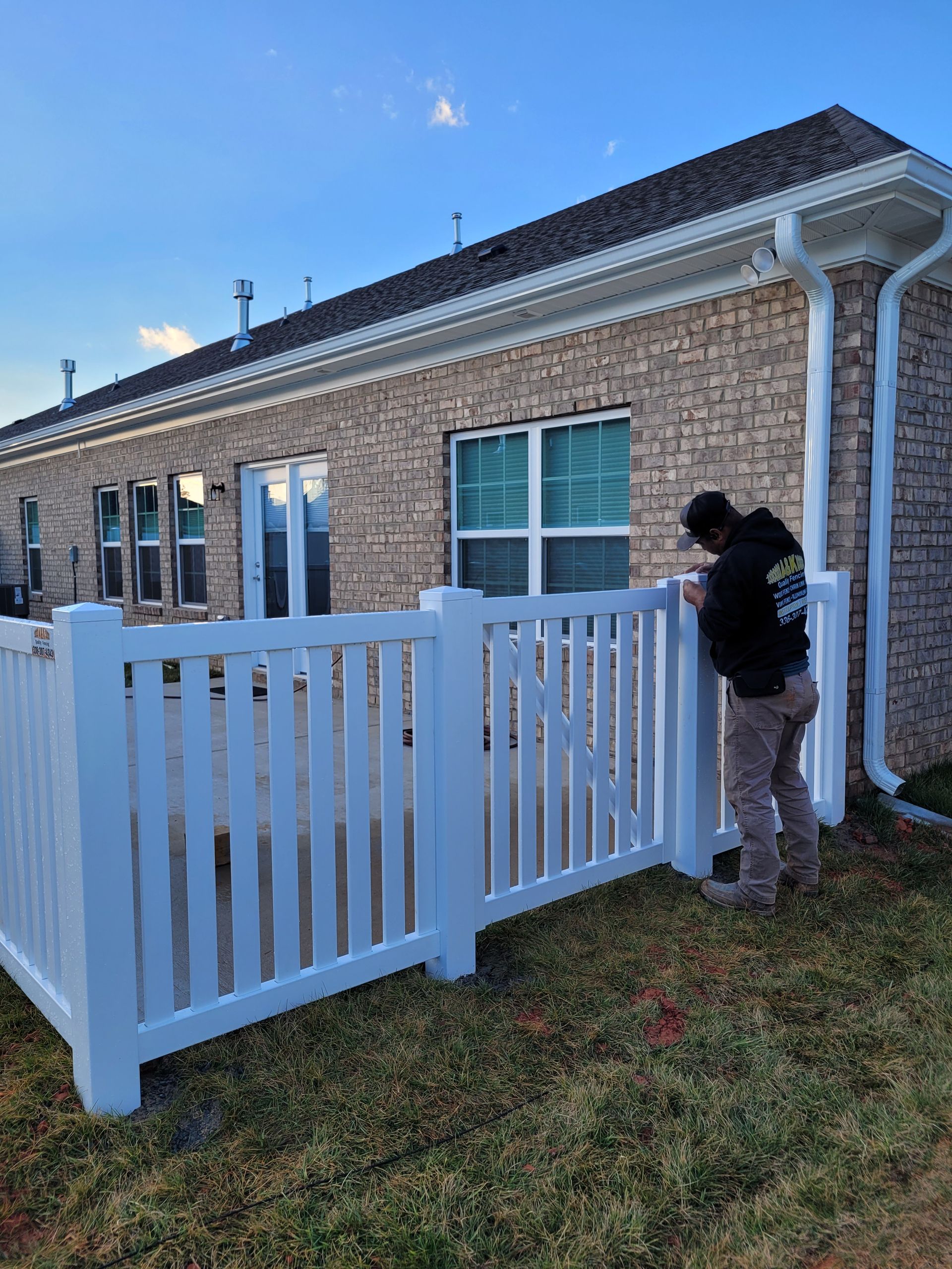 Person installing a white vinyl fence next to a brick building.