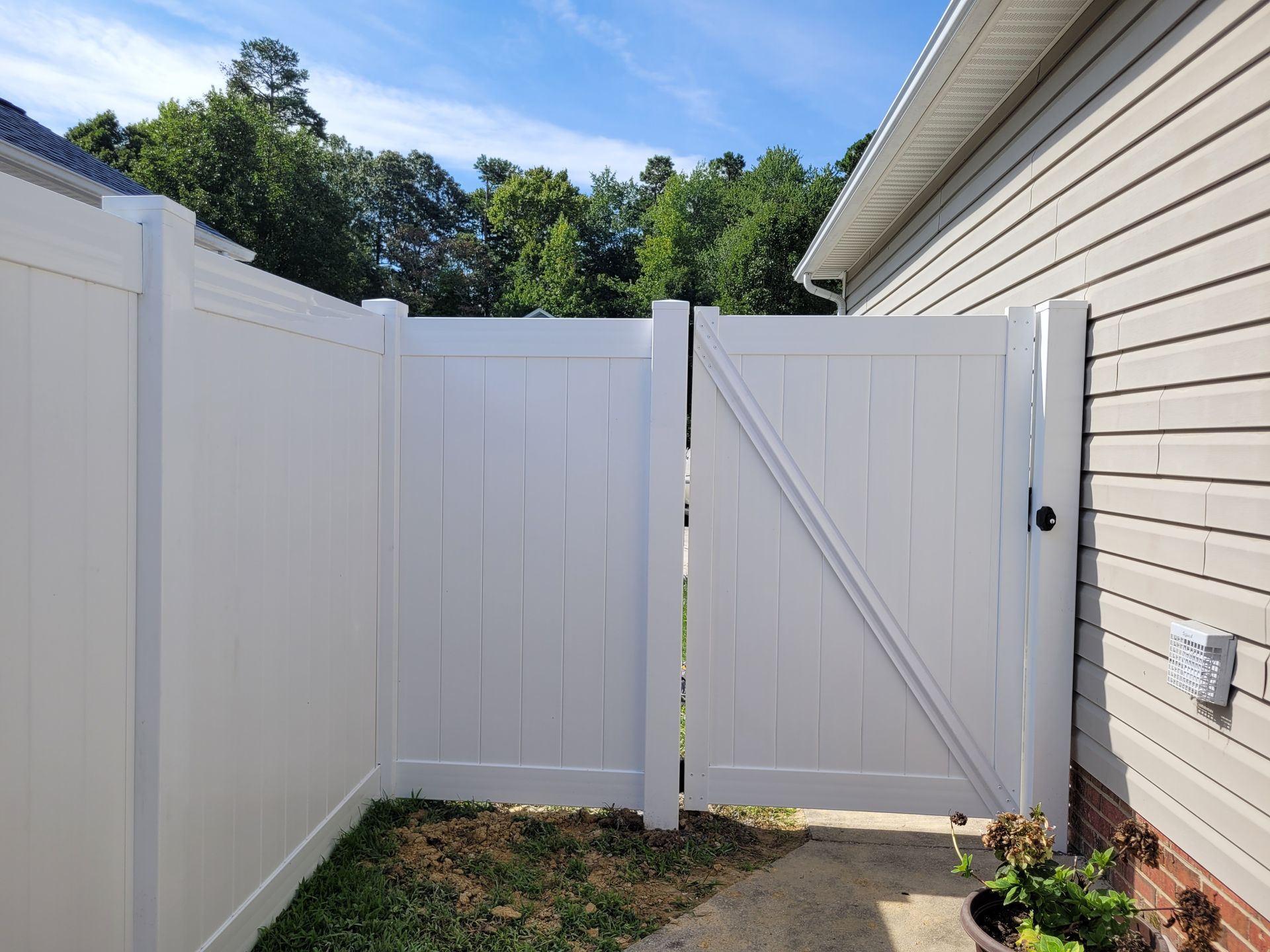 White vinyl fence and gate next to a house, leading to a grassy area under a blue sky.