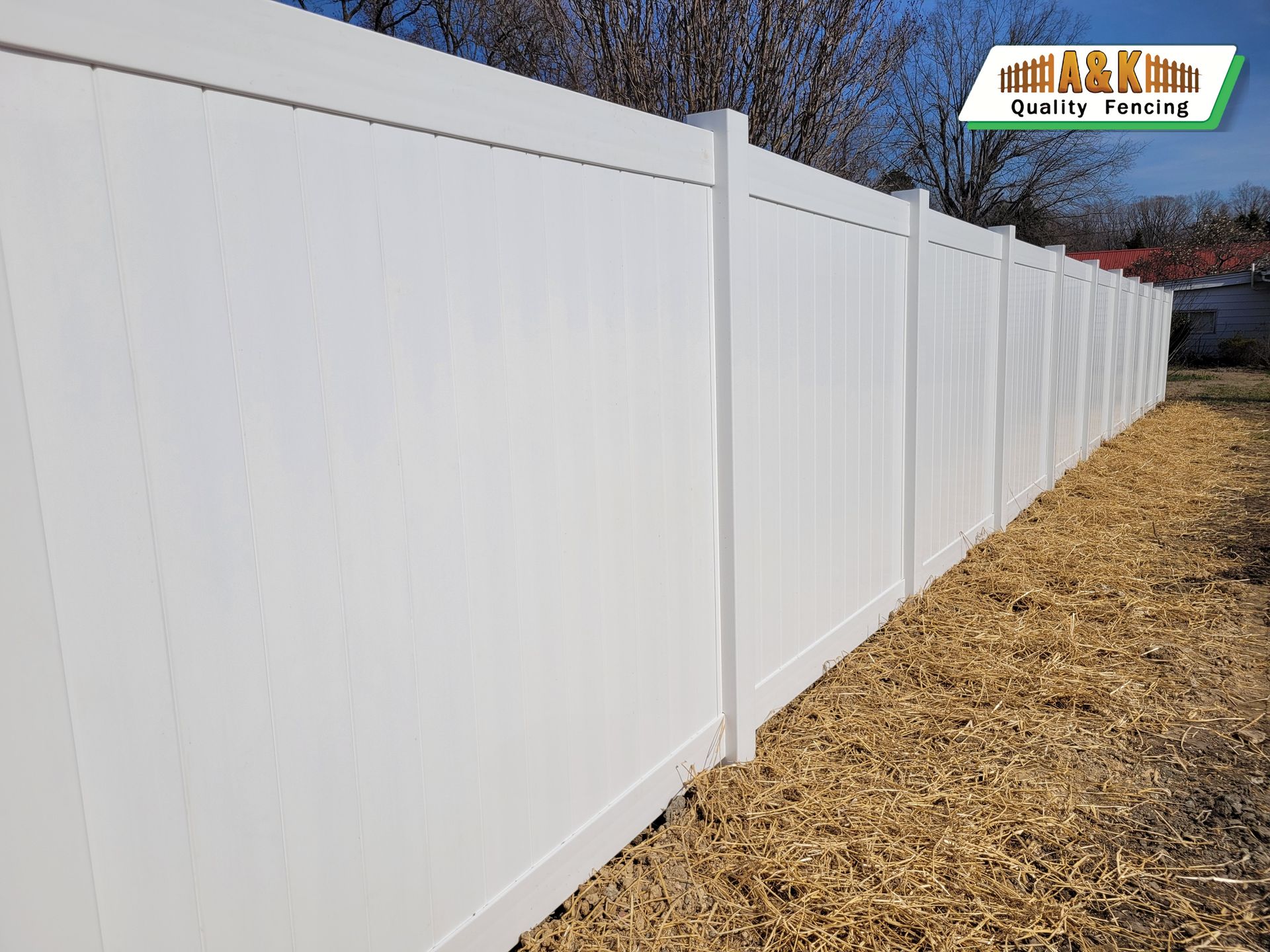 White vinyl privacy fence in a yard with brown gravel ground.