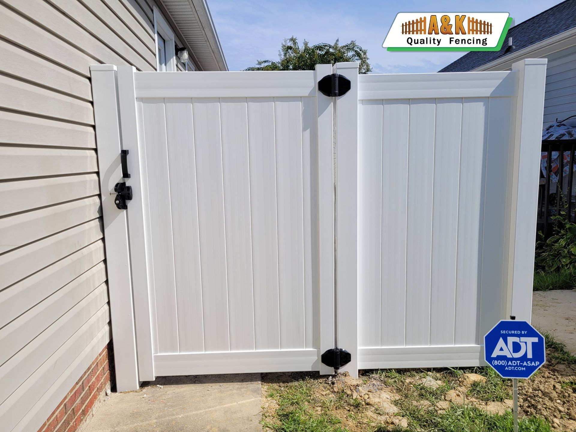 White vinyl gate in a yard, secured with black hardware. House siding visible in background.