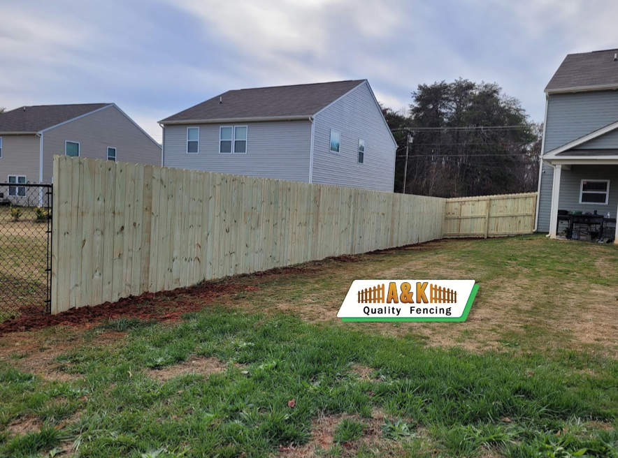 Wooden fence in a backyard, beside a chain-link fence, with houses in the background.