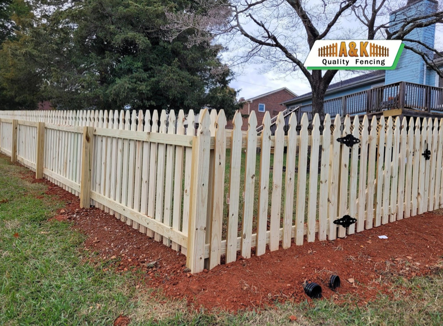 Wooden picket fence bordering a yard with brown mulch and green grass.