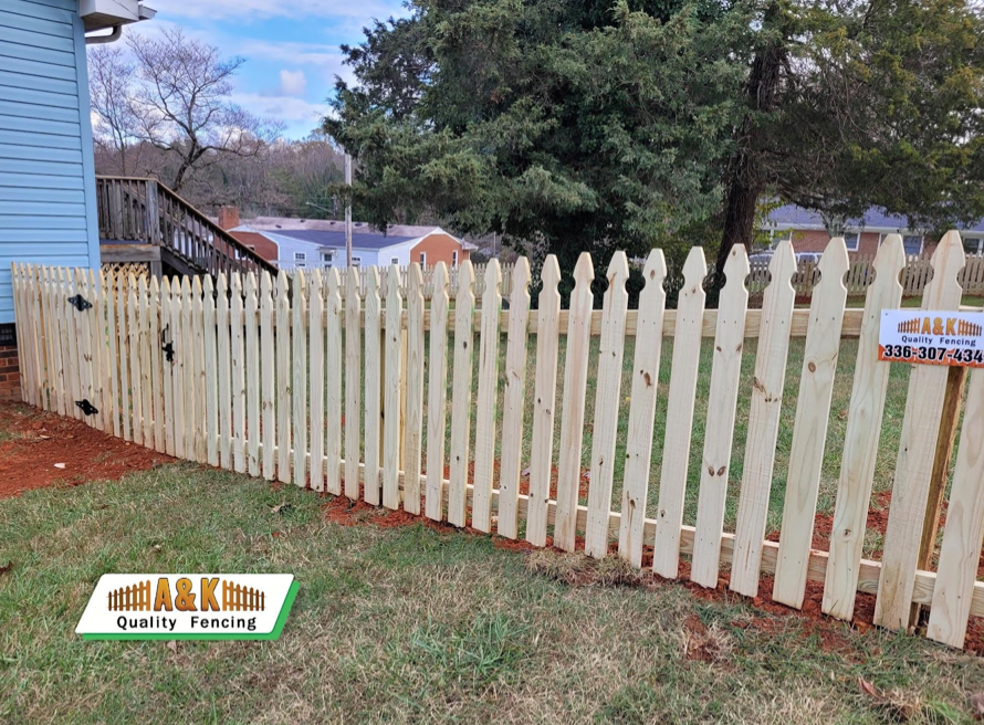 New wooden picket fence with sign, in front of a house and yard.