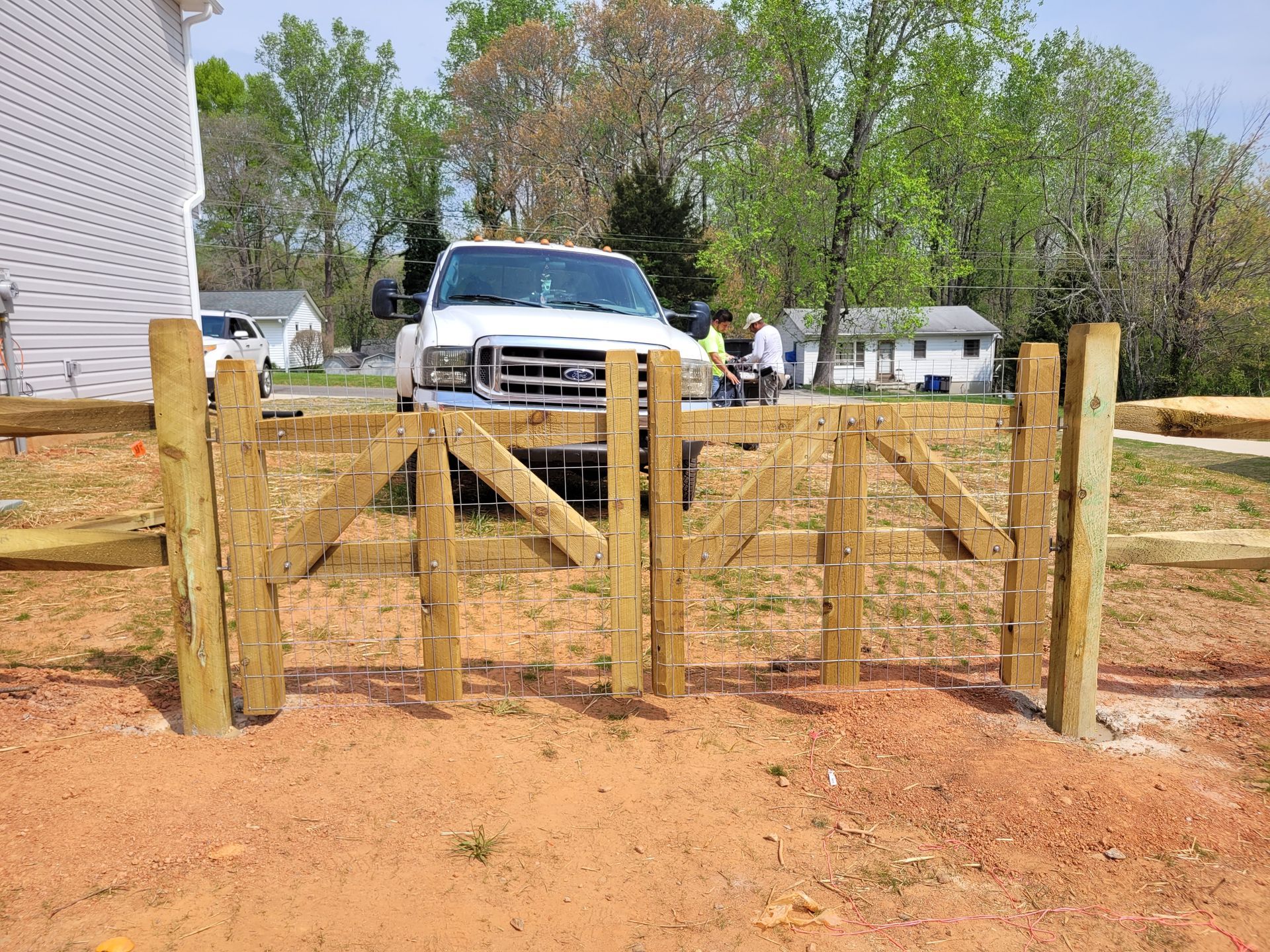 Wooden gate with diagonal braces; truck and houses in the background.