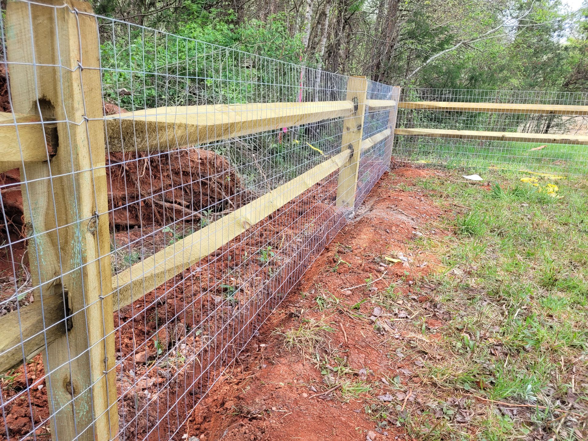 Wooden fence with wire mesh, bordering red dirt and grass.
