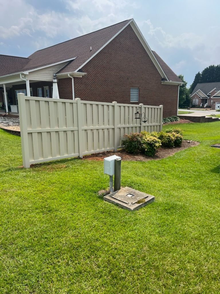 Lawn with a cream-colored fence bordering a brick house and landscaping. A utility box is in the foreground.
