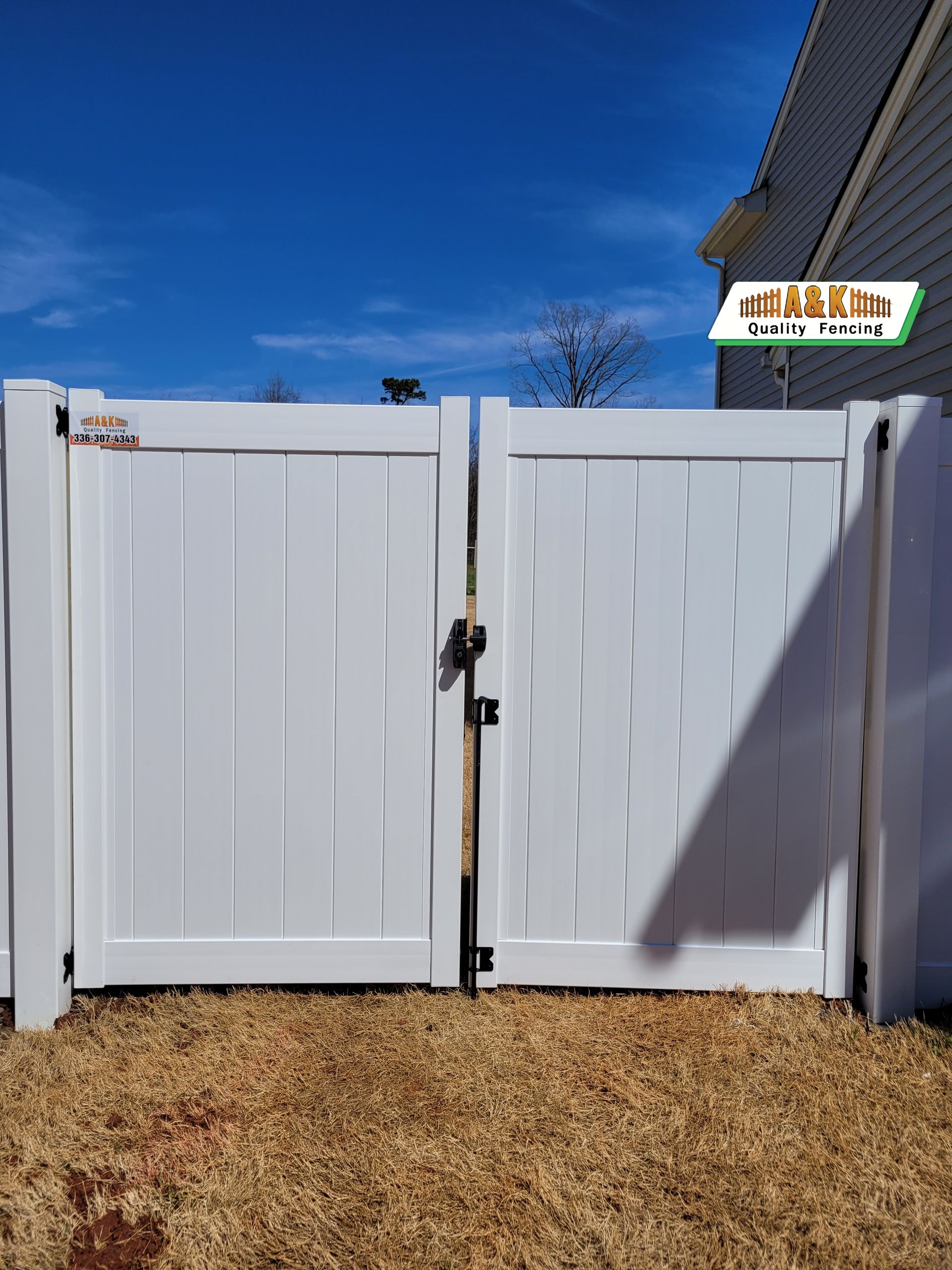 White vinyl fence with closed double gates under a blue sky.