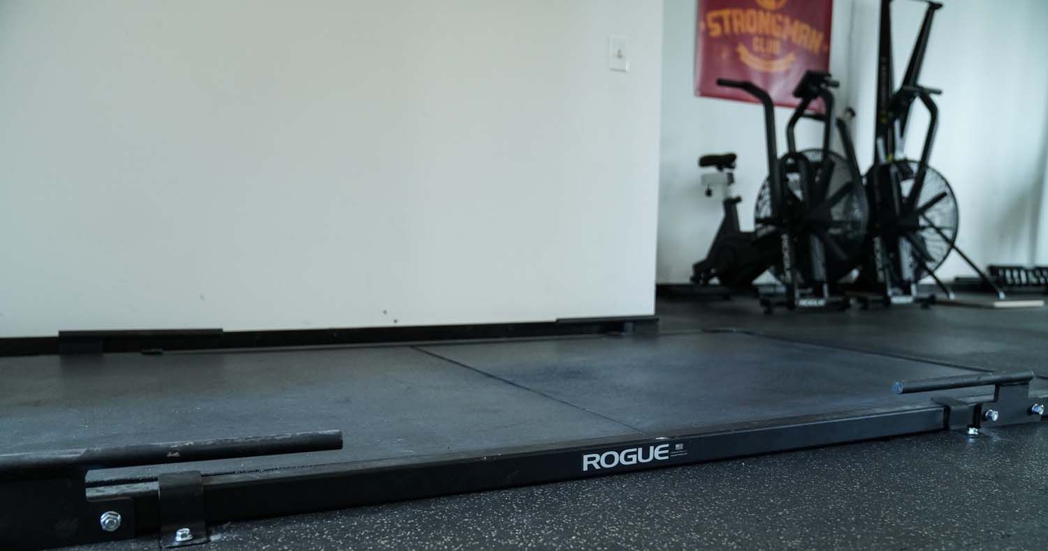 A gym with a lot of exercise equipment and a rogue barbell on the floor.