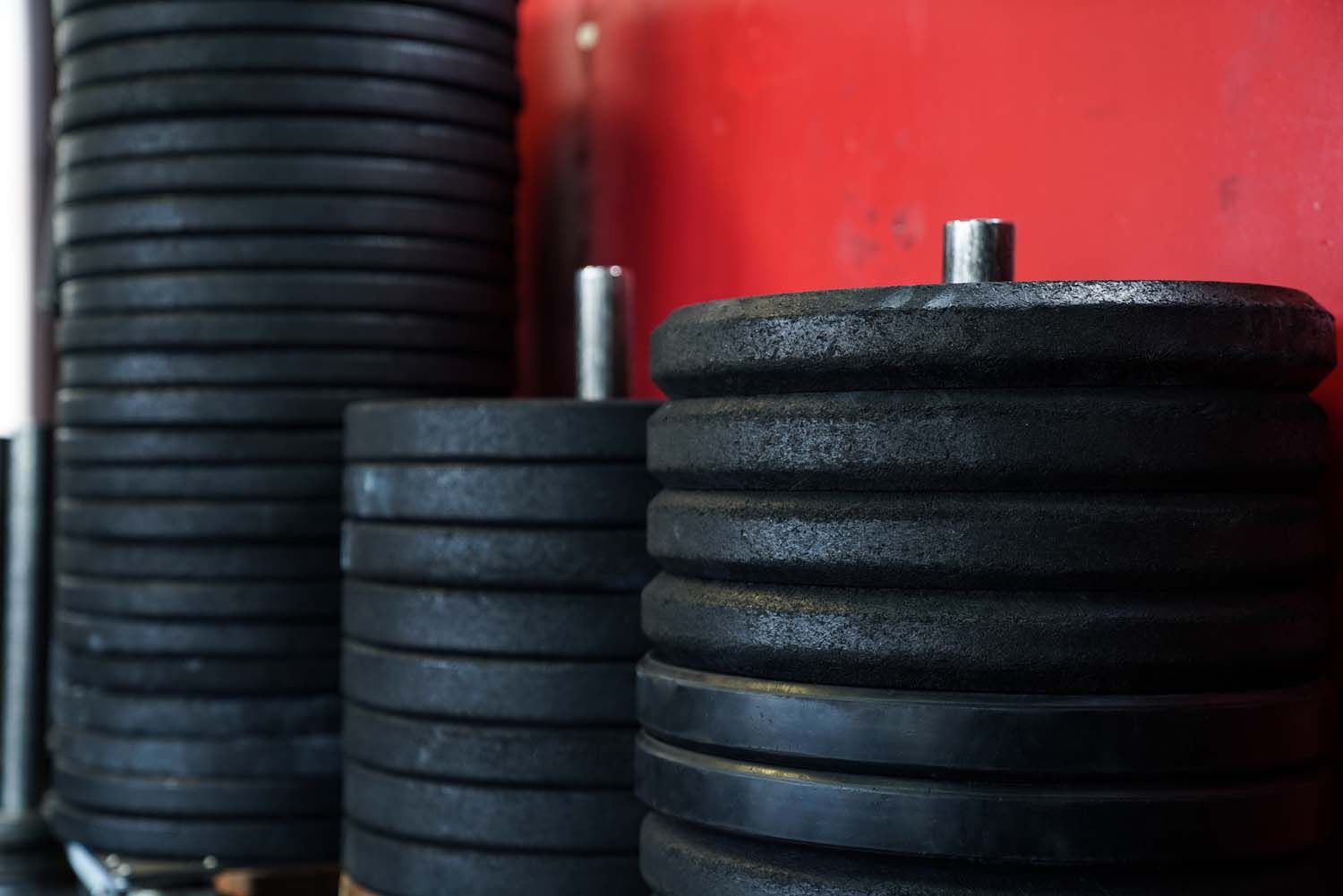 A stack of black weight plates against a red wall.