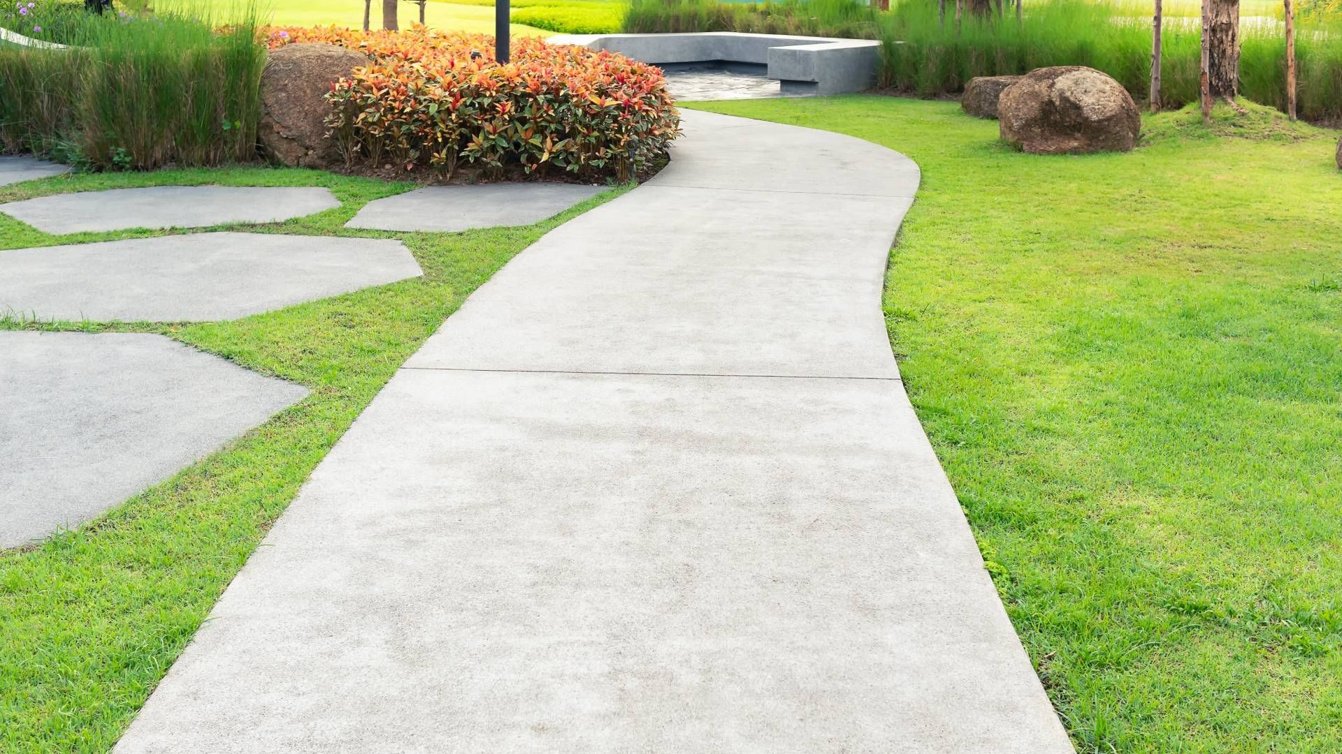 A concrete walkway in a park surrounded by green grass.