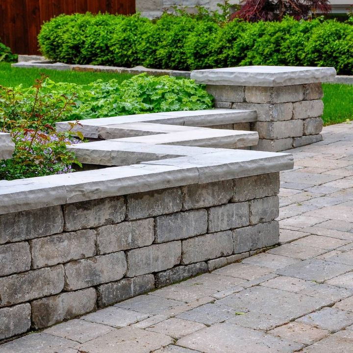 A stone wall with a brick walkway and benches in a garden.
