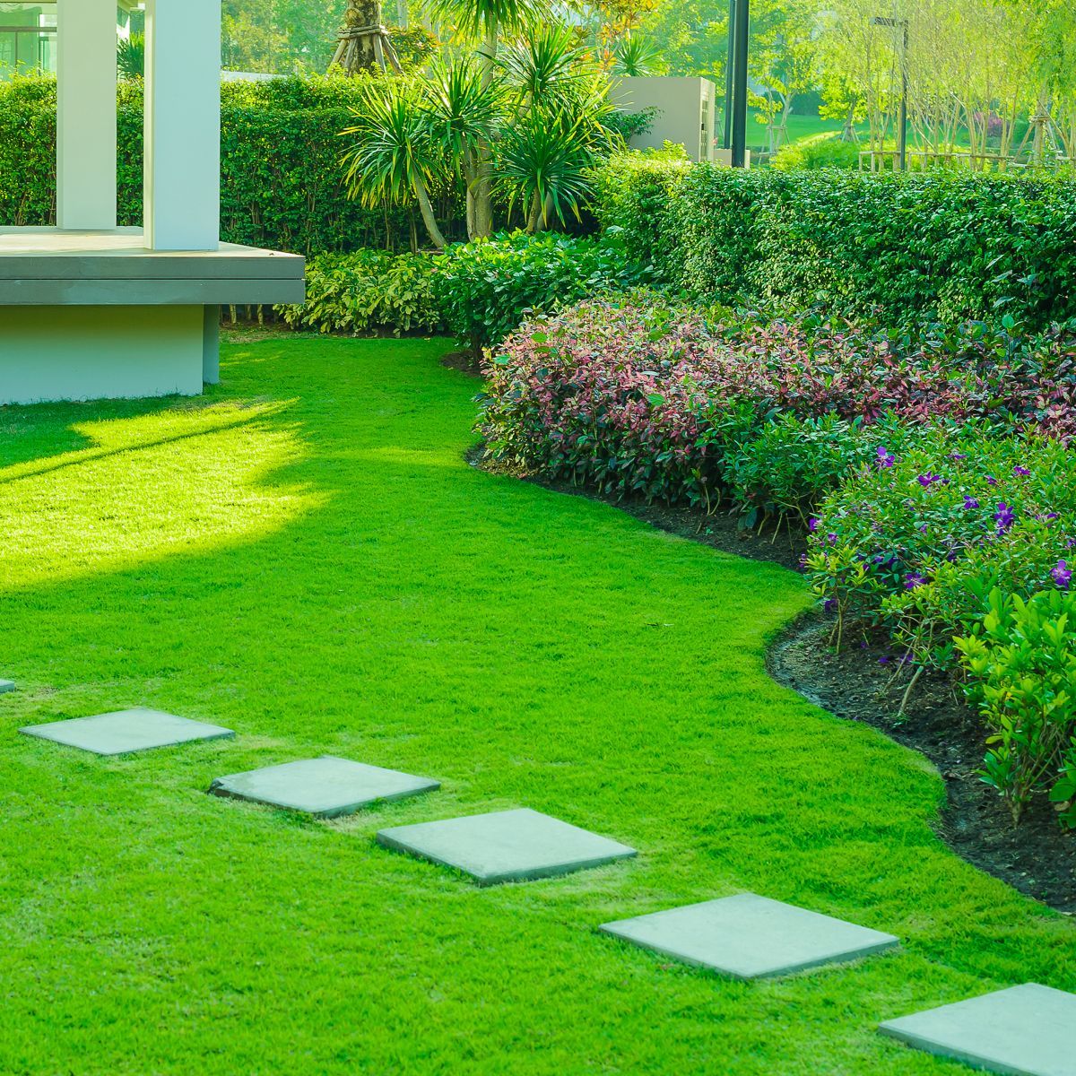 A lush green lawn with stepping stones and flowers in a garden.