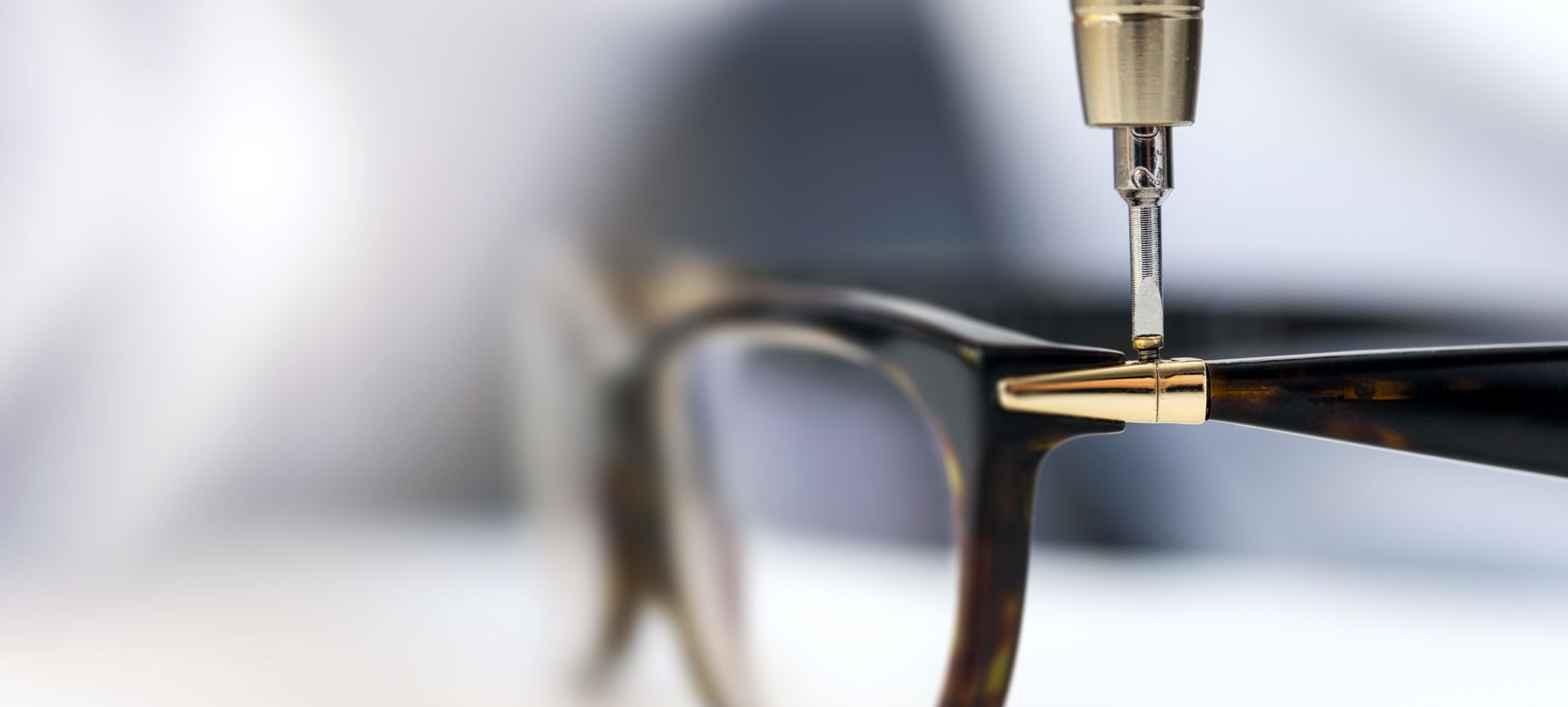 A drill bit making a precise hole in the metal hinge of black eyeglass frames
