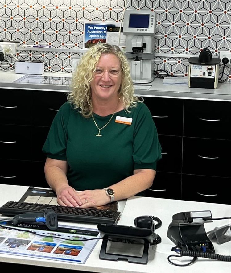 Woman at a counter with equipment; wearing a green shirt, smiling, in a brightly lit setting with patterned wall tiles.